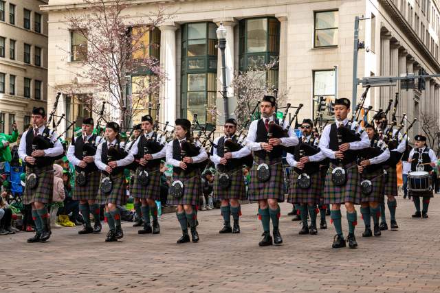 A group of people in Irish attire marching and playing bagpipes in a street parade