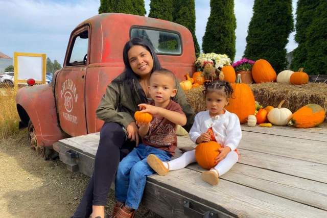 A woman with two small children posing with pumpkins on a tractor at a farm
