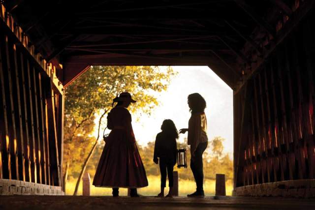 Silhouettes of two adults and a child standing on an old bridge with the sun shining through