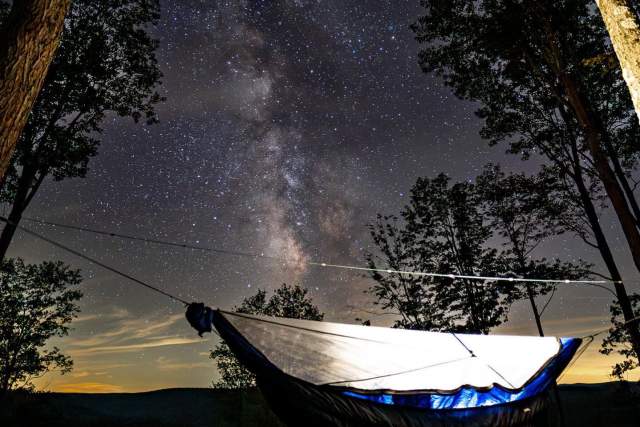 A hammock set up between two trees at night with stars in the sky