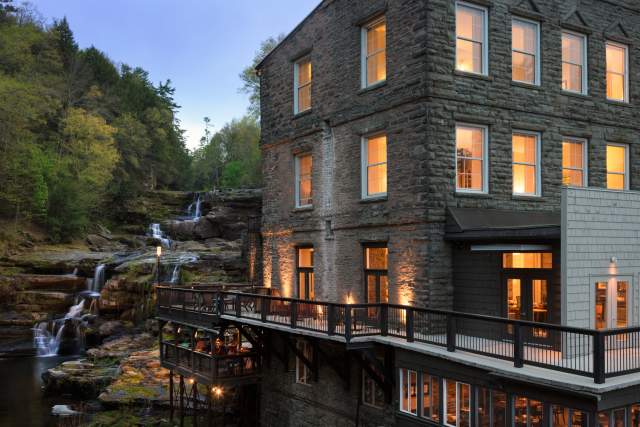 Exterior of a stone hotel with a balcony at dusk that sits overlooking a waterfall