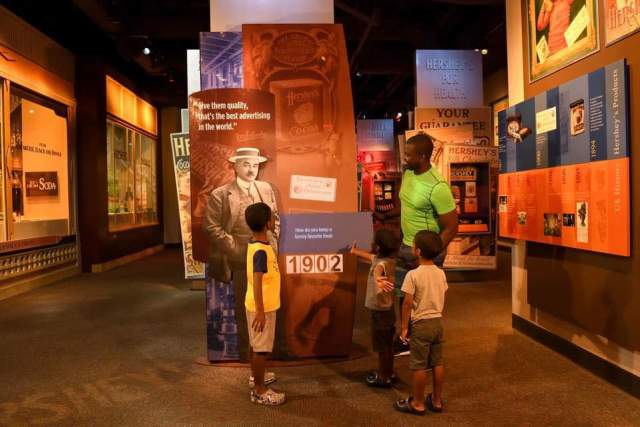 Three kids with an adult enjoying and exhibit at the Hershey Story Museum