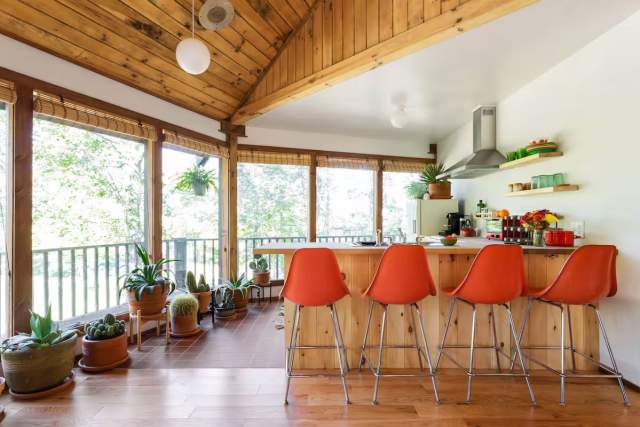 A kitchen in a cabin with orange chairs at the counter and floor to ceiling windows