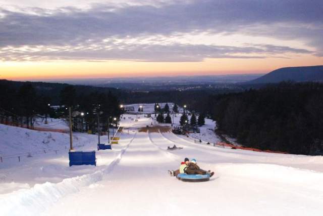 People snowtubing on designated lanes at a snowtubing park at dusk.