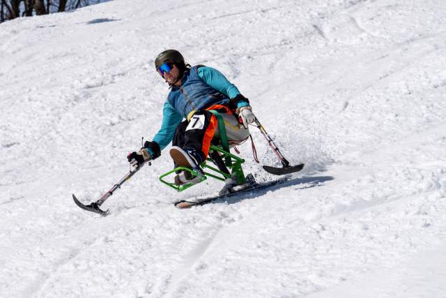 A mobility disabled person skiing down a hill with adaptive gear, including a foot brace and two small poles.