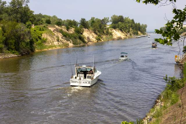 Boats move down a waterway that is lined with vegetation covered dunes.