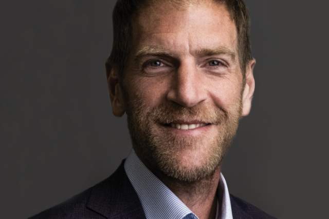 Smiling man in dark grey suit and light blue button up shirt