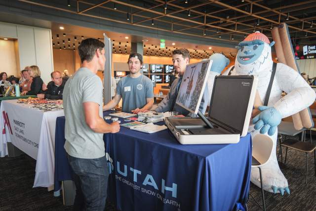 Man standing at a vendor table for Ski Utah speaking to another man behind the table