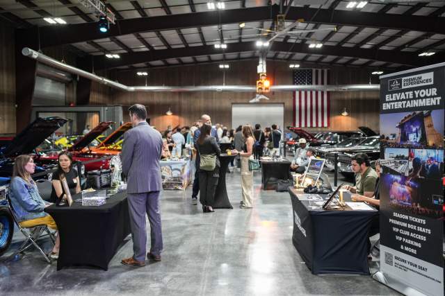 A very clean high end looking garage with custom cars set up for a networking event. People are mingling and talking between the cars