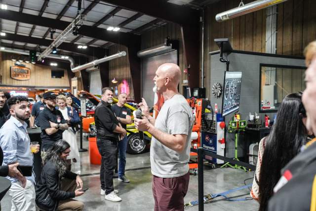 Man addressing a group of people standing in front of a roped off area of a garage