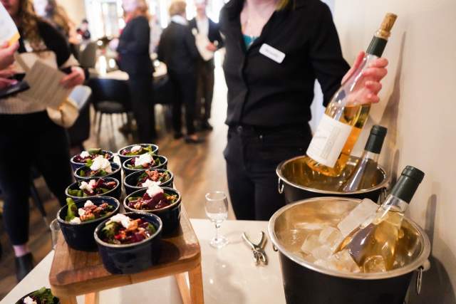 Chilled wine in wine buckets with ice. Small ramekins of salad samples sit on a wooden tray in front of them