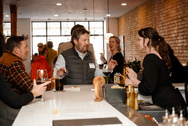 People standing at a bar talking with the bartender and talking to each other
