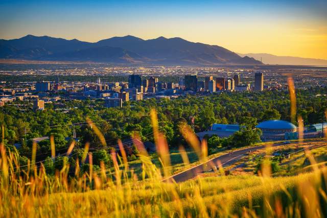 Scenic view of Salt Lake with wild summer grass in the foreground then green trees, then the city  with the mountains and golden light in the background