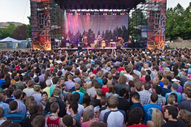 Large crowd of people at the Gallivan Center in front of the stage. It is lit with colored lights and banners on each side that say Twilight Concert Series