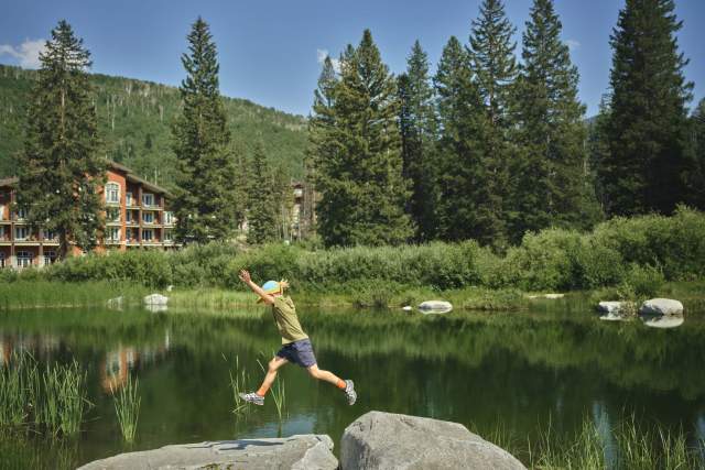 Kid jumping from rock to rock with a mountain lake and lodge in the background