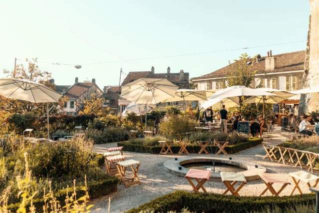 Seating area with umbrellas and garden with swiss buildings in the background