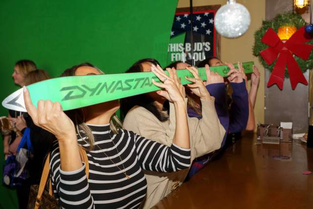 4 people holding a ski up to their faces like they are taking a drink from the shot-ski