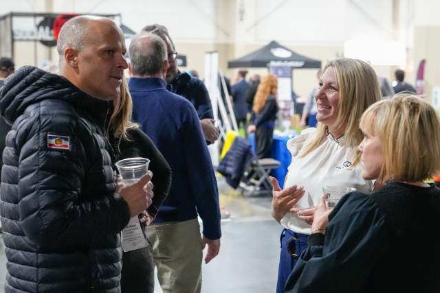 3 smiling people socializing with sports activities and booths in the background