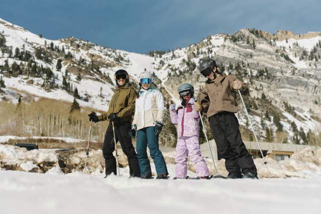 Family of 4 standing on skis with mountains and trees behind them