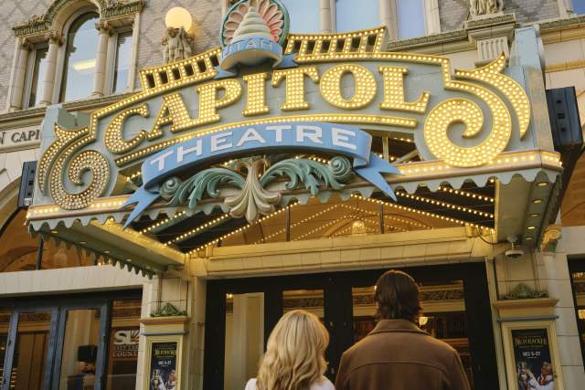 Couple Standing and looking up at a marquee that says Capitol Theatre and has holidya lights and decorations