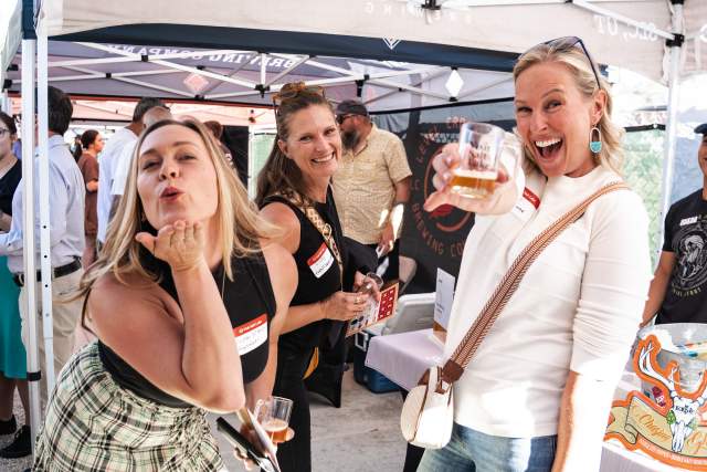 Three girls standing under an outdoor awning smiling and having fun. One of them is blowing a kiss to the camera