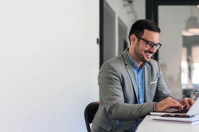 Male business professional in a grey suit working on laptop while sitting at office desk