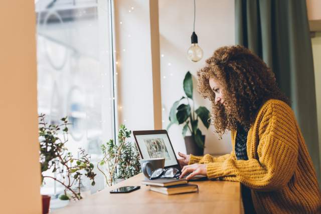 Young woman with curly hair and a yellow sweater working on a laptop