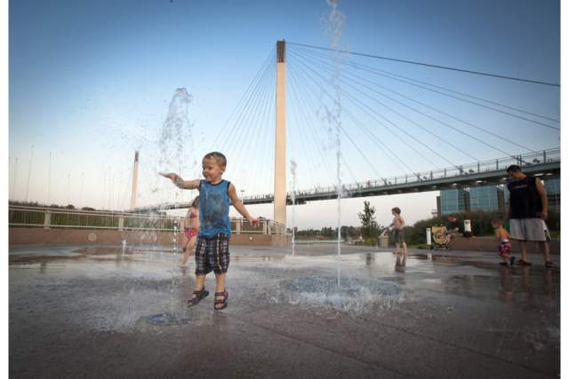 A young child plays on a splash pad with Bob the Bridge in the background.