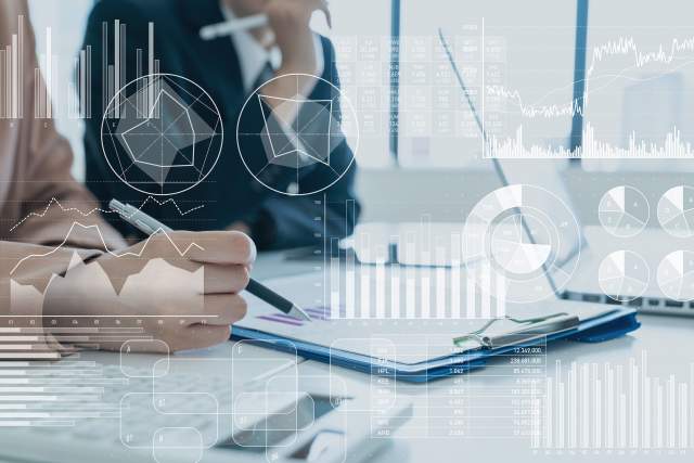 Transparent white graphs and charts on top of a photo of two businesswomen reviewing a clipboard.