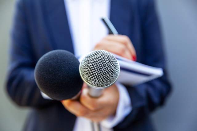 A female journalist takes notes while holding two microphones