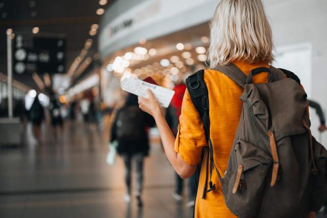 Rear view of a woman at the airport holding a passport with a boarding pass as she walks to her departure gate