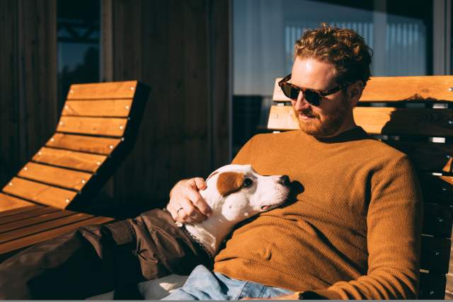 A man lays back on a chair while petting a dog on his lap.
