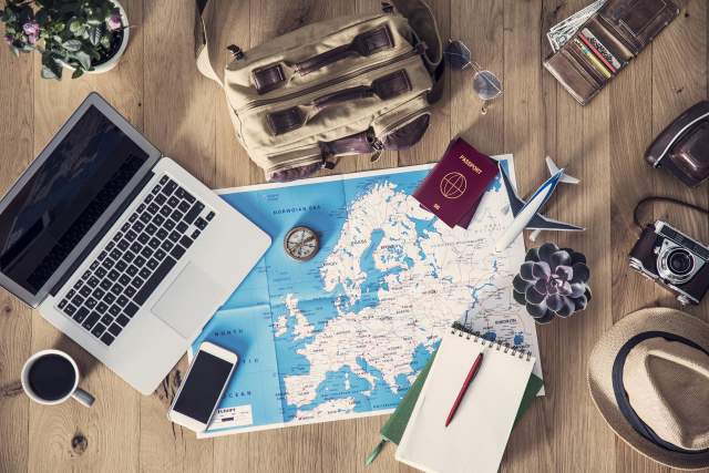 A laptop, cup of coffee, map and compass, among other items, scattered on a table.