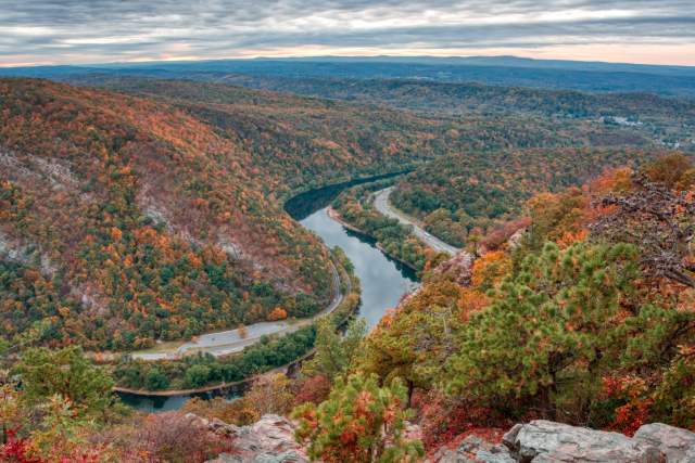 A blue river carves its way through Pocono Mountains covered with trees with leaves of orange, red, and green.