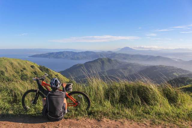 A cyclist stops for a rest and to take in the view at the top of a mountain.