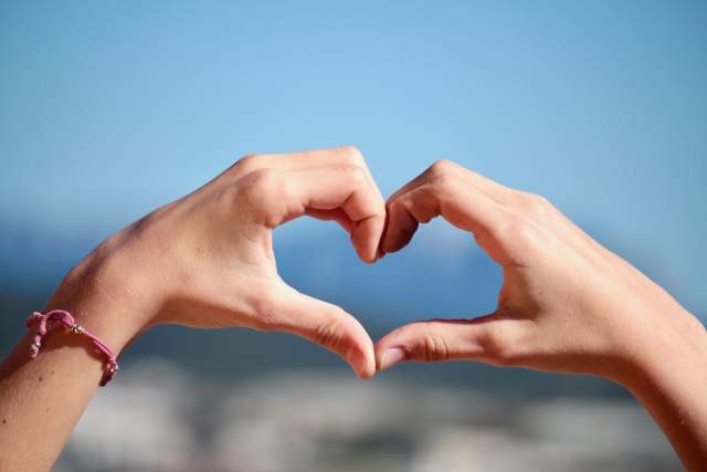 Two hands form a heart in front of blue sky
