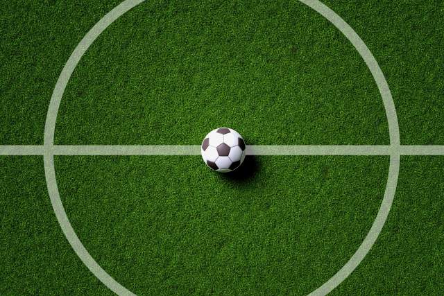 A soccer ball sits at the center circle on a soccer pitch.