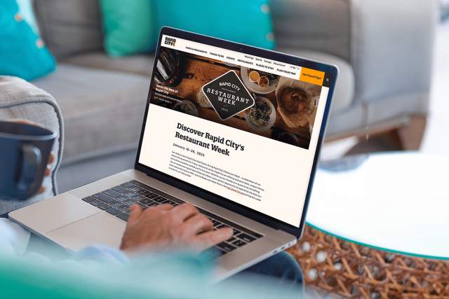 A person holding a coffee mug while browsing the Visit Rapid City website on their Macbook.