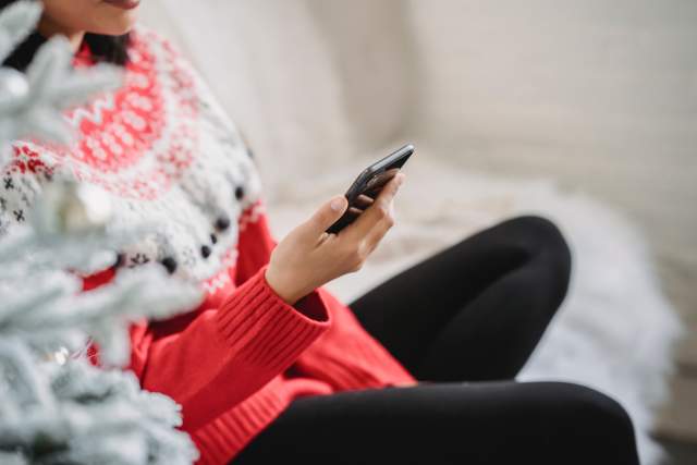 Crop faceless woman using smartphone near Christmas tree
