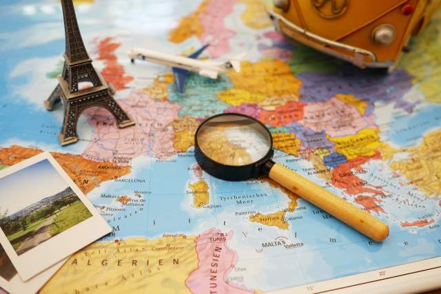 A map of the world on a table with various items such as a magnifying glass and polaroid photos on top of it.