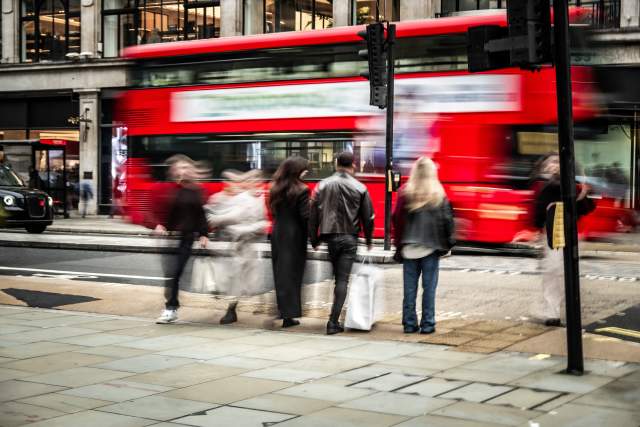 People walking on the sidewalk as a red, two-level bus drives by.