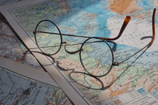 Eyeglasses rest on a table on top of physical maps of the world.