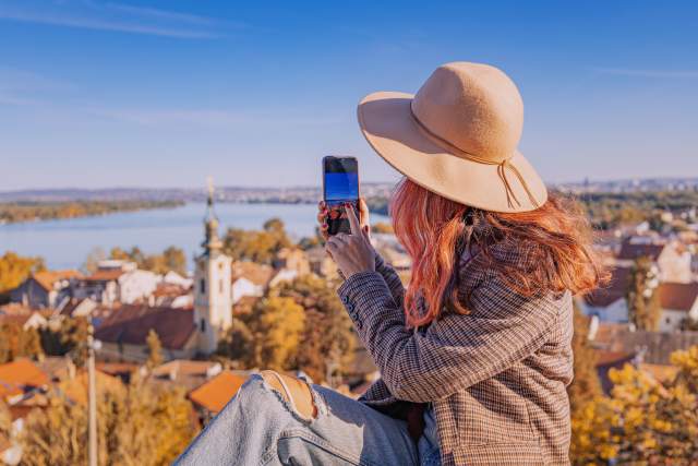 Traveler capturing photos of a historic city and waterfront with a mobile phone.