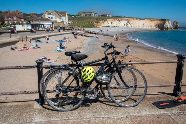 Two bicycles with helmets rest along a seaside promenade overlooking a sandy beach and coastal cliffs, highlighting a destination suited for cycle tourism and outdoor exploration.