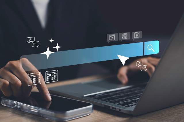 A person working on a laptop computer and mobile phone with a search bar and AI-themed icons overlaid.