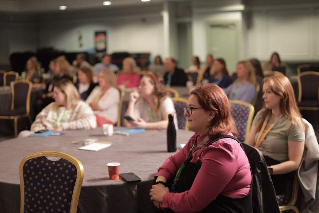 Attendees of the Simpleview 2025 EMEA Summit sit at large, round tables and watch a session.