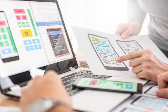 Designers reviewing mobile-first wireframes and prototypes on paper and a laptop screen.