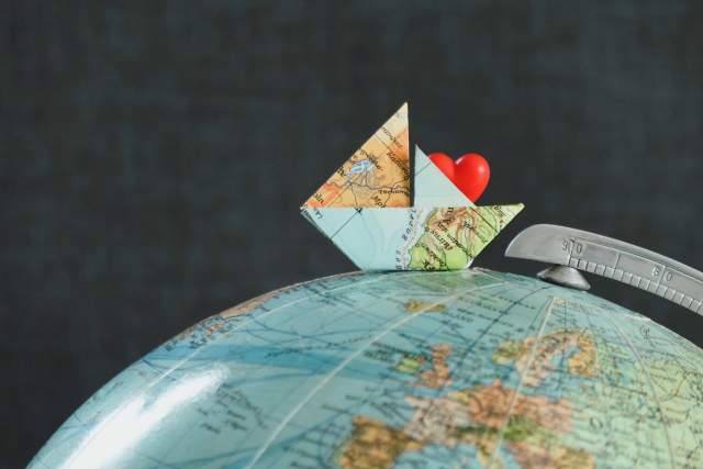 An origami boat made from a world map paper with a red heart inside, placed on top of a globe.