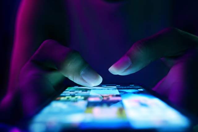 A close up of someone's fingers as they scroll through an Instagram feed on their mobile phone.