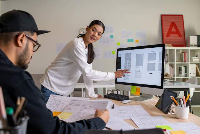 Two designers look over website wireframes and discussing web design.